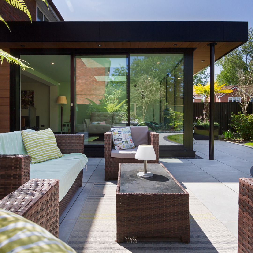 Modern rear garden extension with full-height glazing, outdoor seating area, and landscaped patio connecting indoor living space to a private garden.